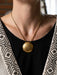 Gold necklace with a large round pendant worn by a person.