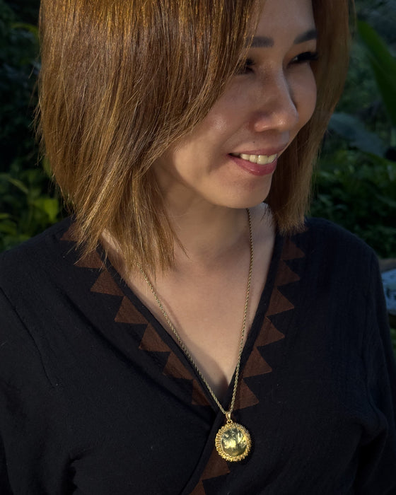Woman wearing a black top with a gold necklace, standing outdoors.
