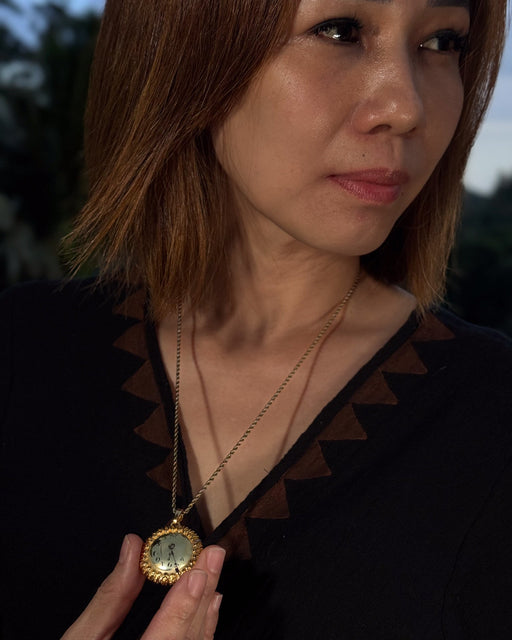 Woman holding a gold necklace with a pendant outdoors