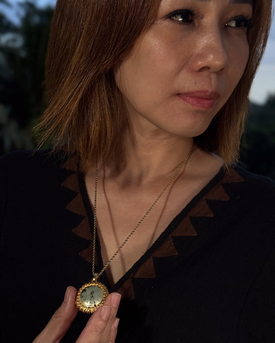 Woman holding a gold necklace with a pendant outdoors