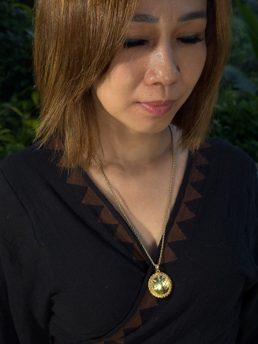 Woman wearing a gold necklace with a pendant outdoors
