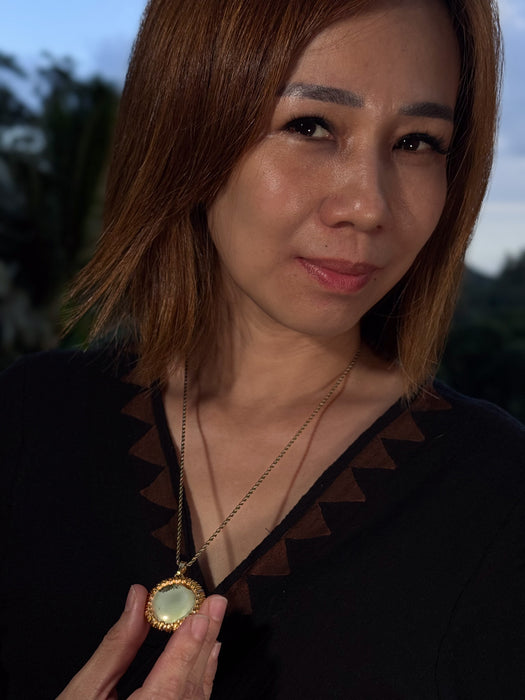 Woman holding a gold necklace with a pendant against a blurred outdoor background