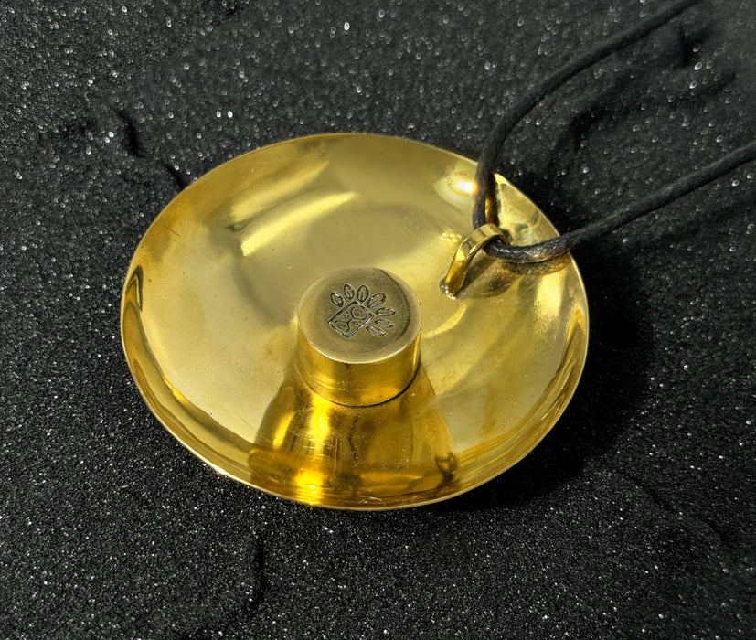 Gold pendant with a black cord on a dark textured background