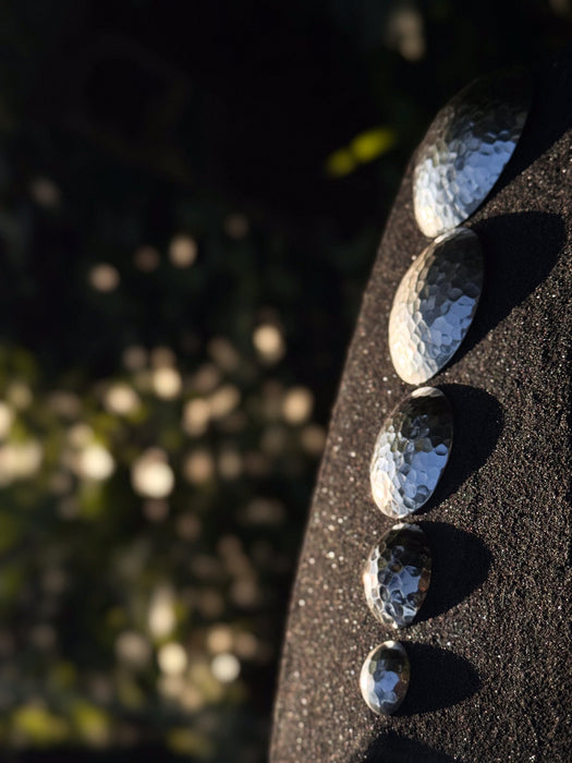 Hammered metal stones arranged on a dark surface with a blurred natural background