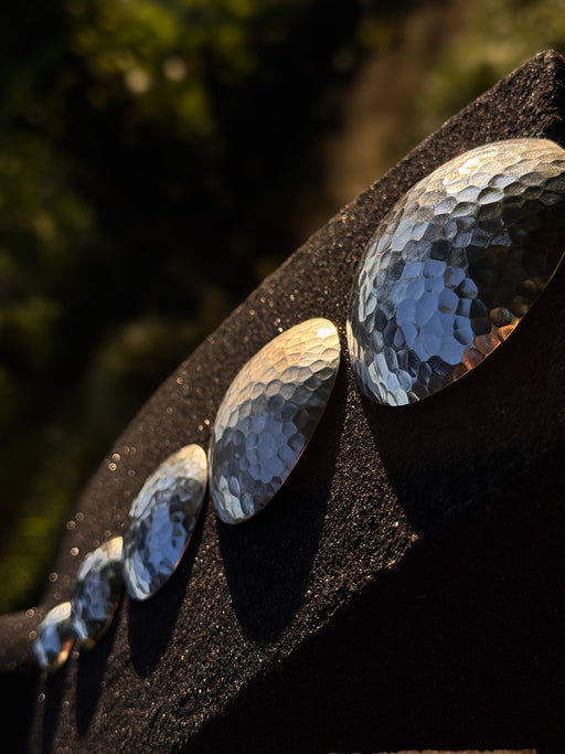 Close-up of metallic oval stones on a dark surface with blurred greenery in the background