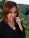 Woman holding a silver pendant outdoors with greenery in the background