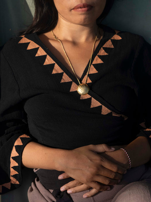 Person wearing a black and brown patterned top with a gold necklace.