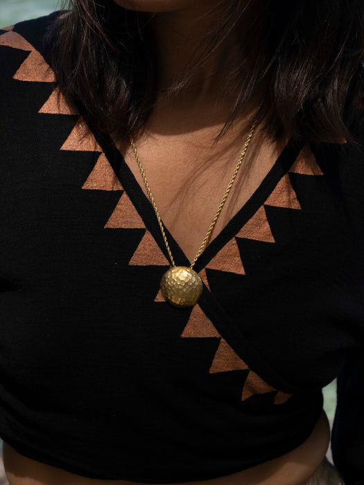 Gold necklace with a spherical pendant on a person wearing a black top with geometric patterns.