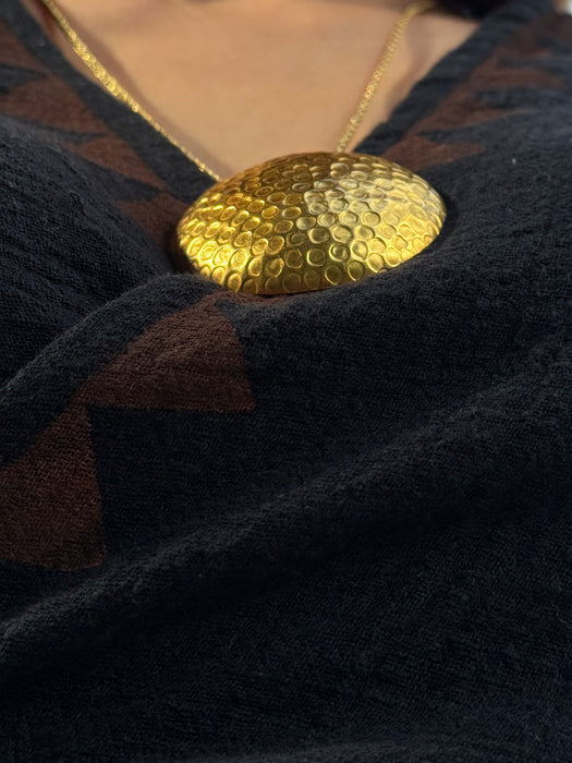 Gold necklace with a textured pendant on a dark fabric background