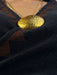 Gold necklace with a textured pendant on a dark fabric background