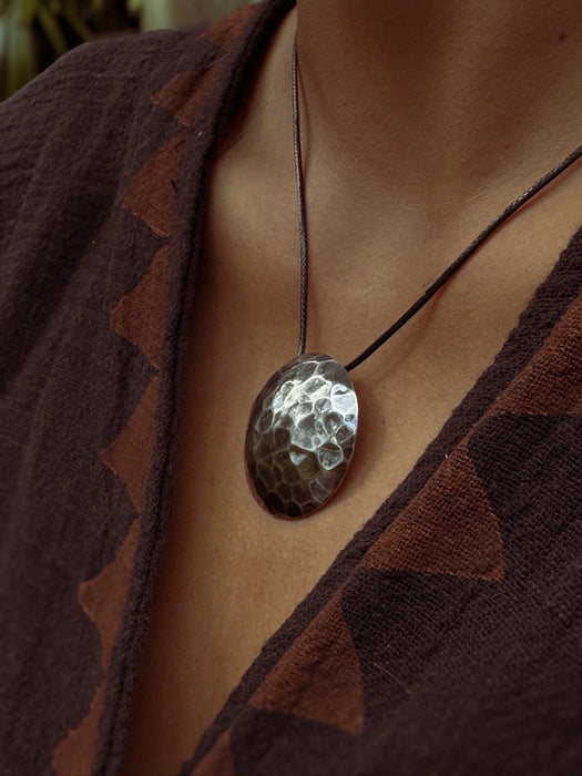 Close-up of a person wearing a textured pendant necklace with a brown patterned garment.