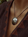 Close-up of a person wearing a textured pendant necklace with a brown patterned garment.