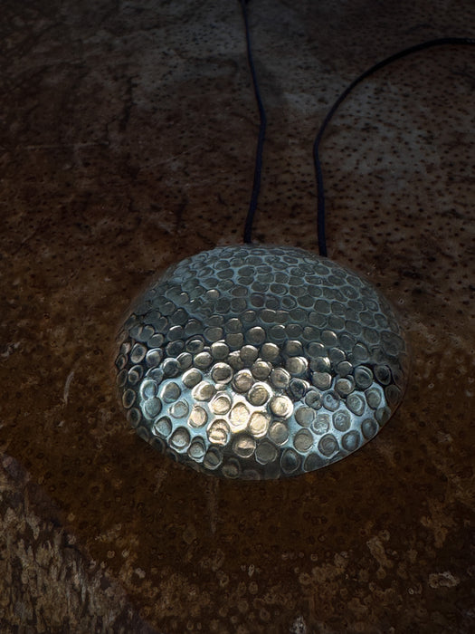 Metallic pendant with textured surface on a dark background