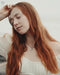 Woman with long red hair wearing a white top against a neutral background