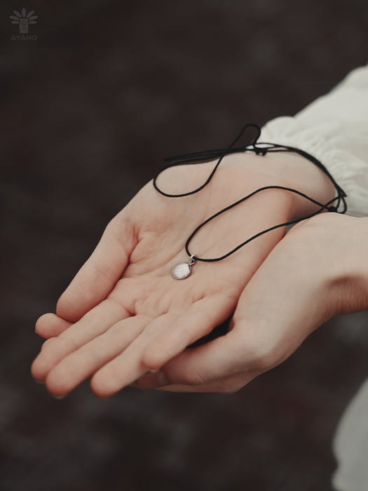 Person holding a black necklace with a pendant on a blurred background