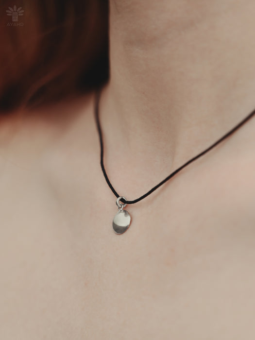 Necklace with a small pendant on a person's neck against a neutral background