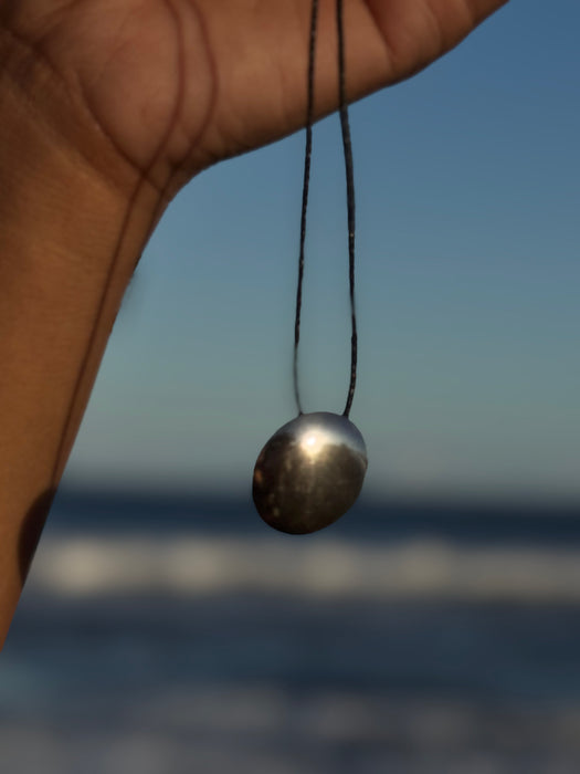 Hand holding a necklace with a silver pendant against a blurred ocean background