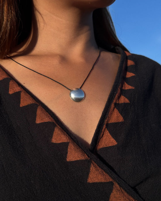 Necklace with a round pendant worn by a person against a blue sky.