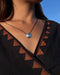Necklace with a round pendant worn by a person against a blue sky.