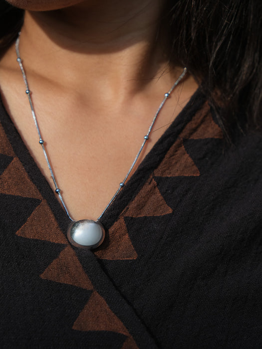 Necklace with a round pendant worn by a person against a dark background