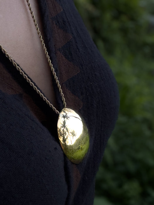 Gold necklace with a pendant on a person wearing a dark jacket against a blurred green background