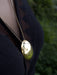Gold necklace with a pendant on a person wearing a dark jacket against a blurred green background