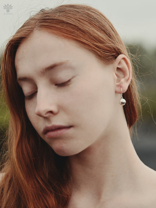 Close-up of a person with red hair wearing a pearl earring.