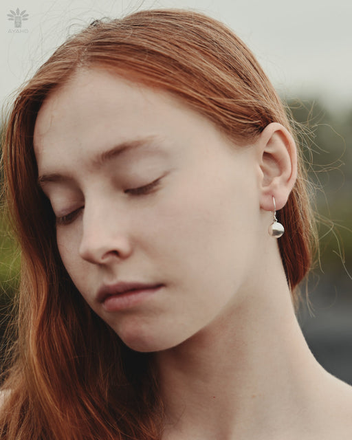 Close-up of a person with red hair wearing a pearl earring.