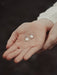 Silver earrings held in a person's hand against a dark background