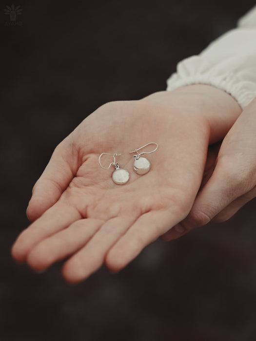 Silver earrings held in a person's hand against a dark background