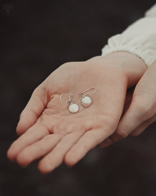 Silver earrings held in a person's hand against a dark background