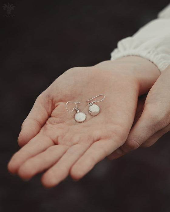 Silver earrings held in a person's hand against a dark background