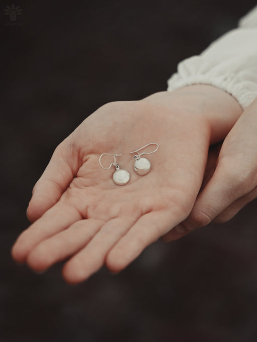 Silver earrings held in a person's hand against a dark background