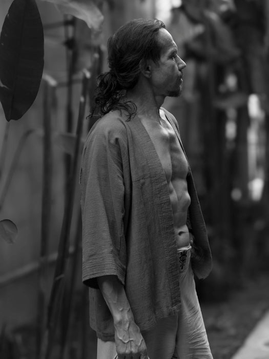 Man with long hair and a beard standing outdoors in black and white.