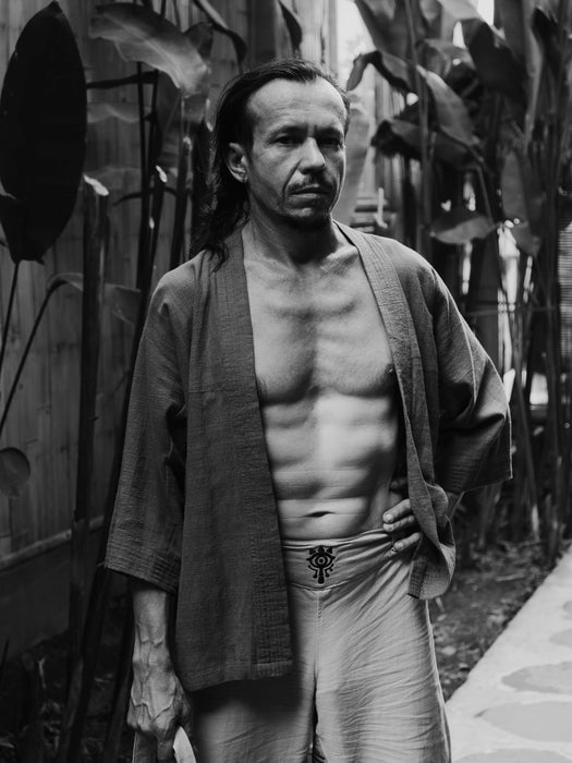 Man in traditional Japanese attire standing outdoors with plants in the background