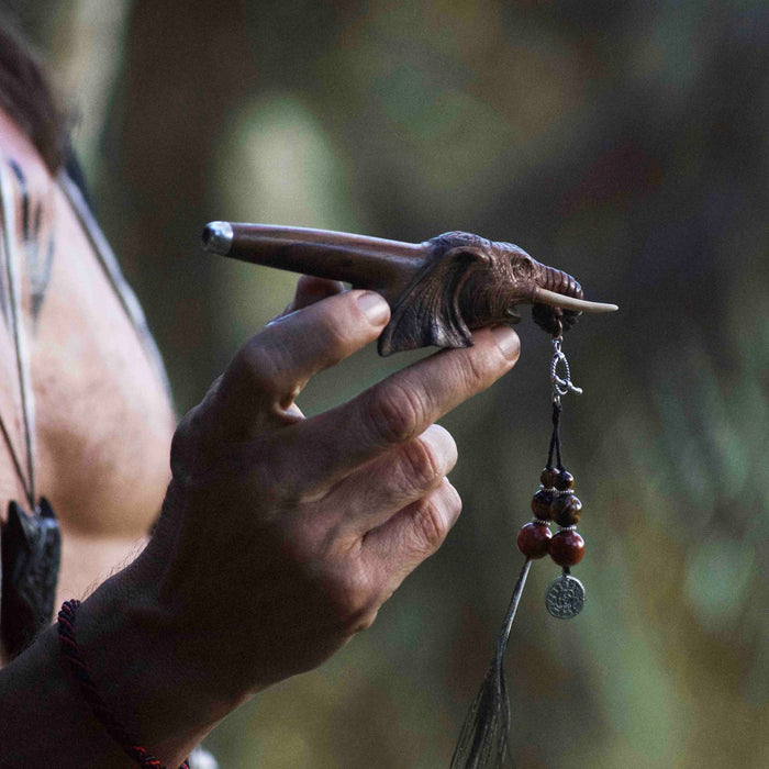 a wooden kuripe elephant pipe, designed for hape snuff application. The kuripe, linked to a charm-adorned necklace, serves as a unique, handmade smoking accessory and part of a shamanic protection kit, blending herbal medicine traditions