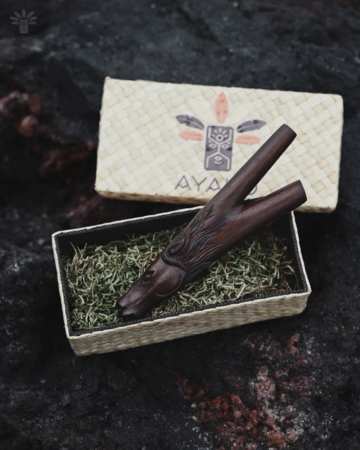 Wooden smoking tool on a bed of green moss with 'AYA' branding in the background