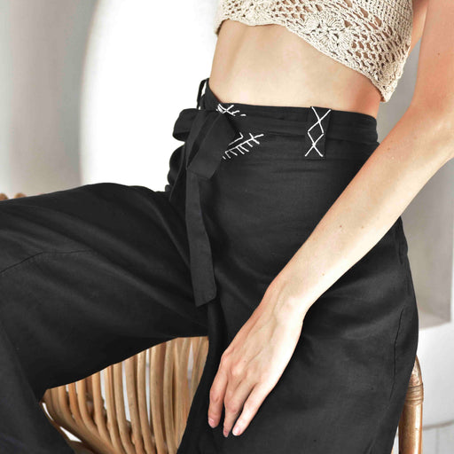 Close-up of unisex black linen pants featuring a white hand-embroidered tribal pattern, paired with a delicate crochet top, embodying Boho and shamanic styles