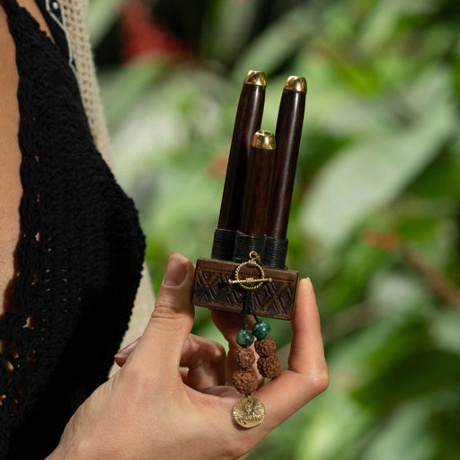 Rose wood kuripe pipe necklace with a protective Shipibo ornament, presented on a carved wooden hand, symbolizing high-quality shamanic heritage
