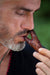 A handcrafted wooden kuripe pipe, with intricate shamanic designs, is held against a blurred green background. This unique gift, also used as a hape snuff applicator, is part of a larger collection of herbal medicine smoking accessories