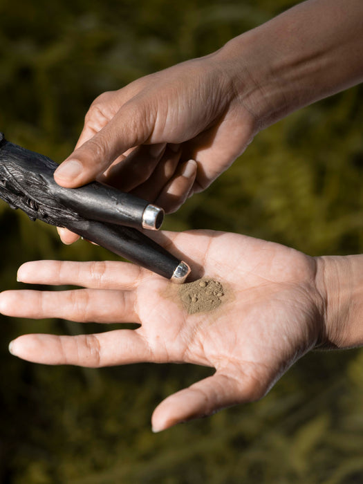Hand holding a small object with another hand against a natural background