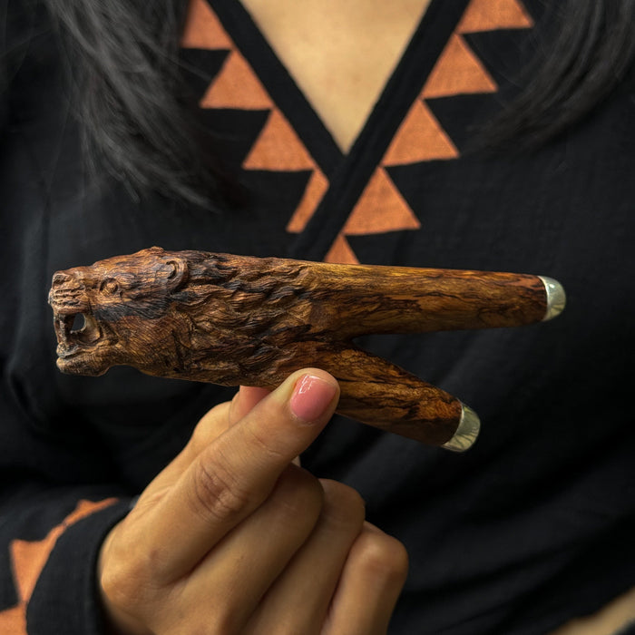 Hand holding a wooden object with intricate carvings against a patterned background