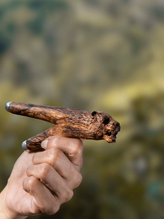Hand holding a wooden tool against a blurred natural background
