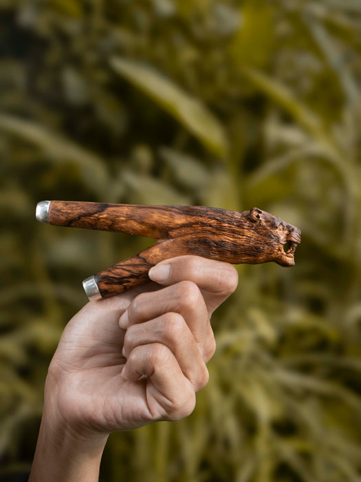 Hand holding a wooden tool against a blurred natural background