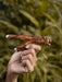 Hand holding a wooden tool against a blurred natural background
