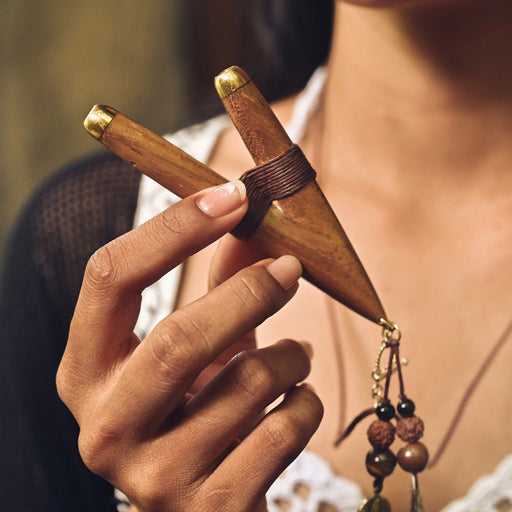 A serene woman holds a high-quality wooden kuripe blowpipe, used as a hape snuff applicator. The kuripe, doubling as a necklace with detailed charms, represents both a shamanic tool and a unique gift.