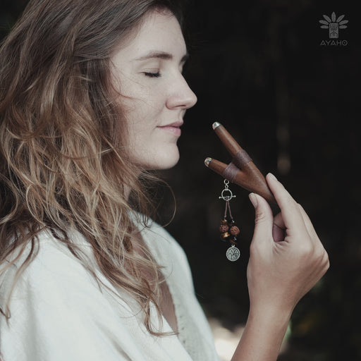 A serene woman holds a high-quality wooden kuripe blowpipe, used as a hape snuff applicator. The kuripe, doubling as a necklace with detailed charms, represents both a shamanic tool and a unique gift.
