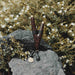 Palm wood kuripe pipe necklace, poised on volcanic rock against a blooming backdrop, merges traditional shamanic utility with a unique handcrafted charm.