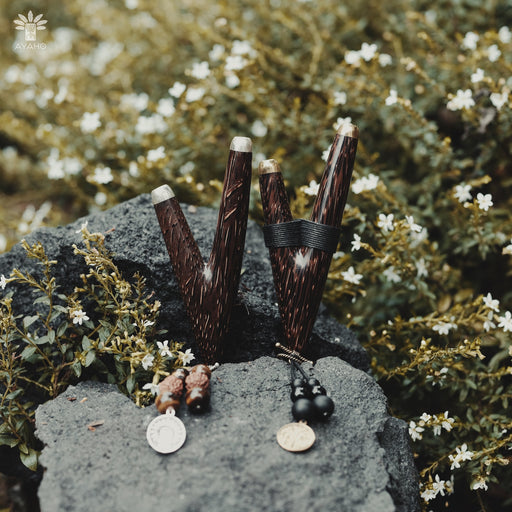 Palm wood kuripe pipe necklace, poised on volcanic rock against a blooming backdrop, merges traditional shamanic utility with a unique handcrafted charm.