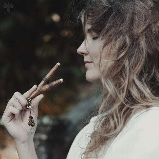 A serene woman holds a high-quality wooden kuripe blowpipe, used as a hape snuff applicator. The kuripe, doubling as a necklace with detailed charms, represents both a shamanic tool and a unique gift.